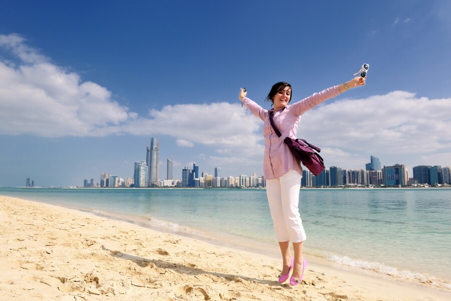lady on a beach in Abu Dhabi looking back at the abu dhabi skyline Abu Dhabi Travel Planner
